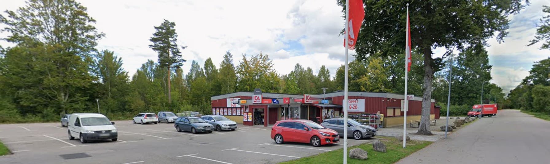 ICA Liatorp sedd från parkeringen, med flaggorna och skogen bakom butiken
